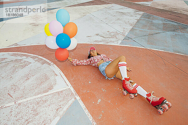 Lächelnde Frau mit Rollschuhen und bunten Luftballons auf dem Sportplatz