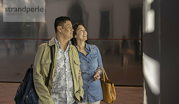 Lächelndes älteres Paar vor beleuchtetem Informationsschild