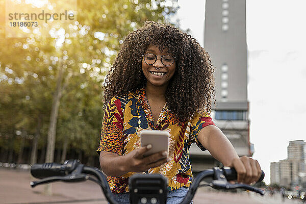 Glückliche junge Frau  die auf dem Fahrrad sitzt und ihr Smartphone benutzt