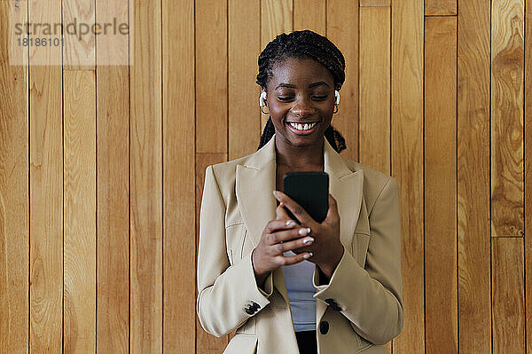 Junge Geschäftsfrau blickt vor einer Holzwand auf ihr Mobiltelefon