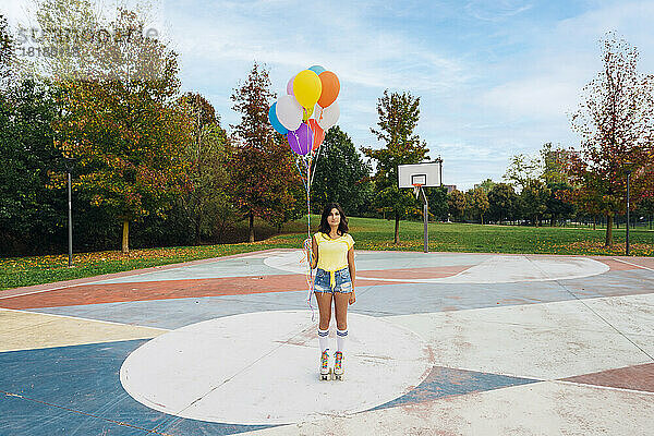 Frau trägt Rollschuhe und hält bunte Luftballons auf dem Sportplatz