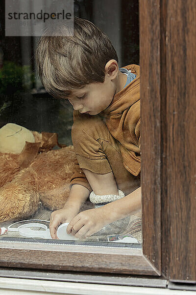 Junge sitzt zu Hause  gesehen durch Glasfenster