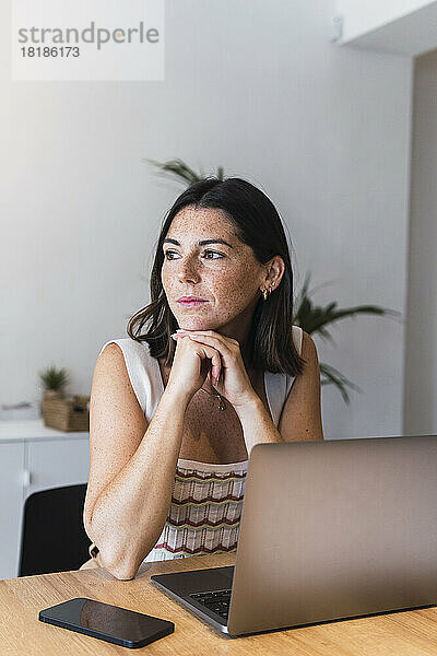 Nachdenkliche junge Geschäftsfrau sitzt vor dem Laptop im Büro