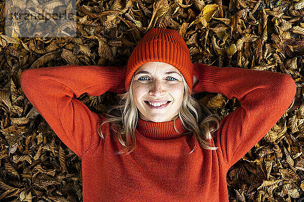 Lächelnde reife Frau mit blauen Augen  die auf Herbstblättern liegt