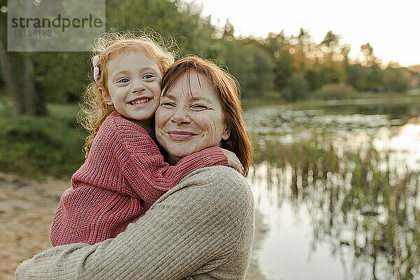 Lächelndes Mädchen umarmt Großmutter am See