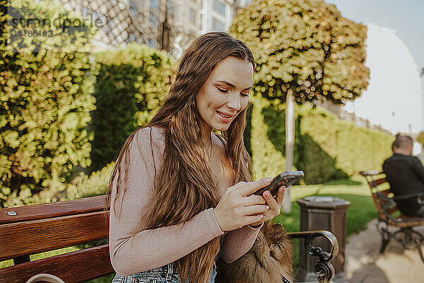 Glückliche Frau benutzt Smartphone auf Bank im Park