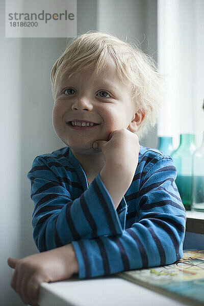 Porträt eines lächelnden kleinen Jungen mit der Hand auf seinem Gesicht