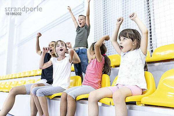 Fröhliche Schüler und Lehrer sitzen auf dem Schulsportplatz