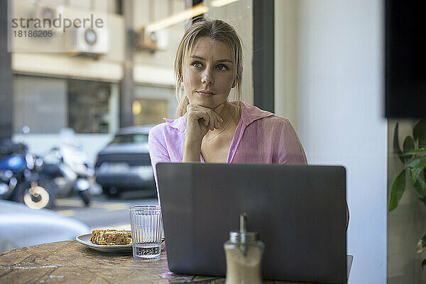 Nachdenklicher Freiberufler sitzt mit Laptop im Café