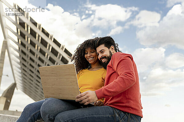 Glückliches junges Paar benutzt Laptop unter bewölktem Himmel