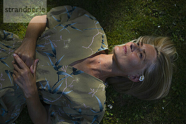 Contemplative mature woman lying in garden