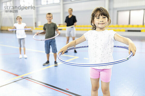Lächelndes Mädchen mit Hula-Hoop-Reifen steht am Schulsportplatz