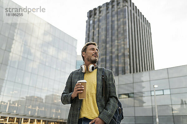 Nachdenklicher Mann mit Einwegkaffeetasse vor dem Gebäude
