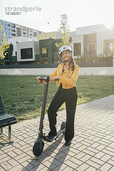 Happy young woman standing with electric push scooter on sunny day