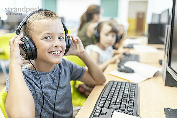 Smiling boy wearing wired headphones in computer class at school