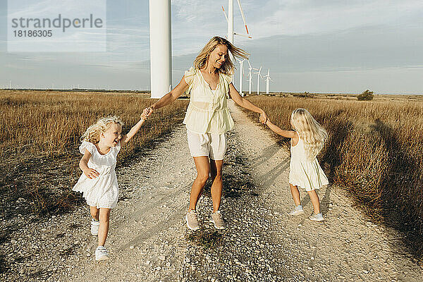 Fröhliche Frau genießt und spielt mit ihren Töchtern an einem sonnigen Tag auf dem Feld