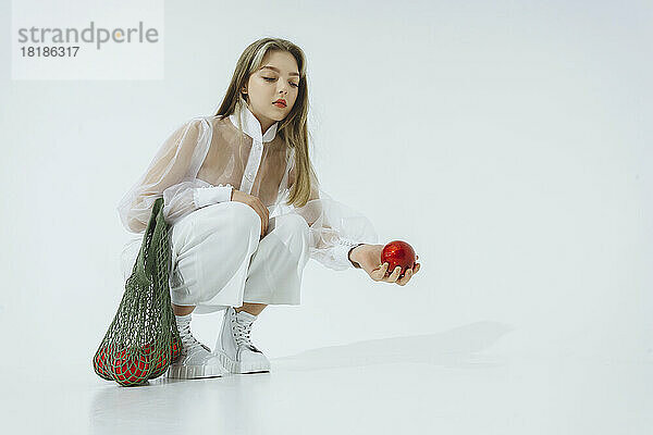 Teenage girl holding Christmas ornament crouching against white background