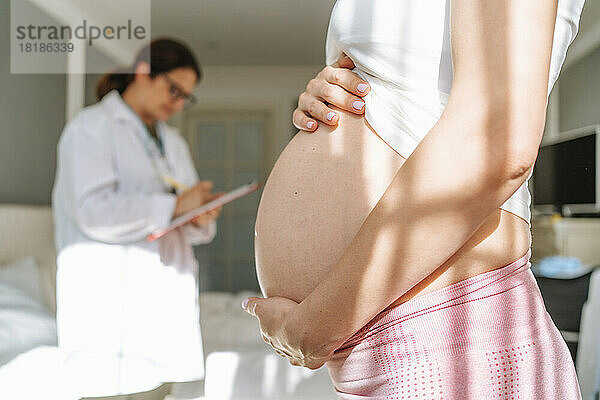 Schwangere Frau berührt Bauch an sonnigem Tag zu Hause