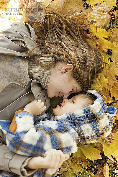Woman lying with son on yellow autumn leaves in park