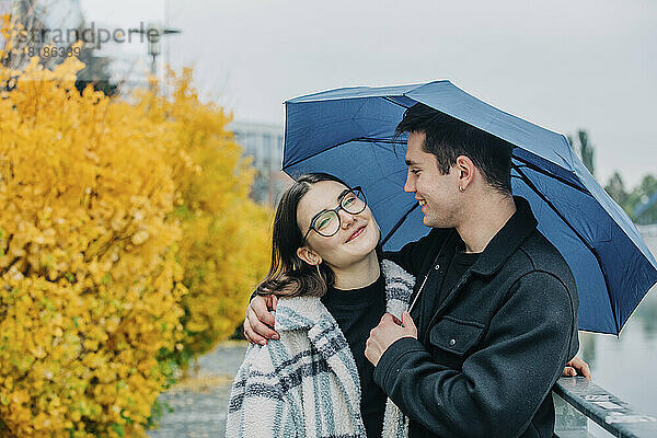 Lächelnder junger Mann und Frau unter Regenschirm im Herbst