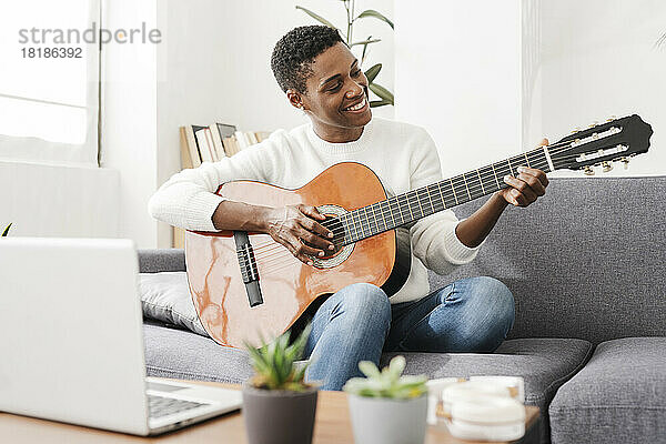 Frau spielt Gitarre auf der Couch mit Laptop auf dem Tisch