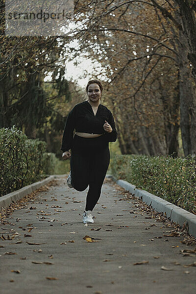 Lächelnde Frau läuft auf Fußweg im Herbstpark