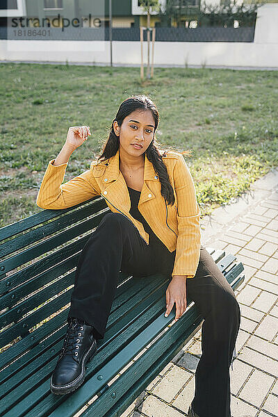 Selbstbewusste junge Frau sitzt auf einer Parkbank