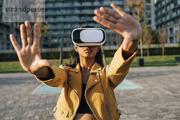 Junge Frau gestikuliert an einem sonnigen Tag mit einem Virtual-Reality-Simulator
