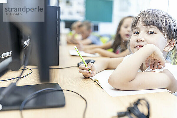 Girl holding pencil leaning on notebook in classroom