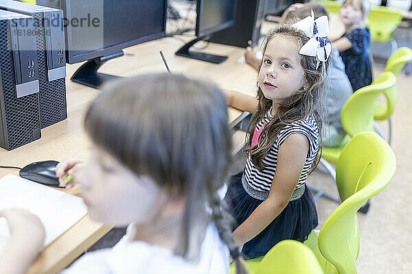 Mädchen sitzt mit Freunden am Schreibtisch im Klassenzimmer der Schule
