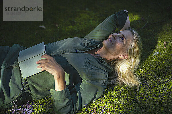 Contemplative woman lying on grass in garden