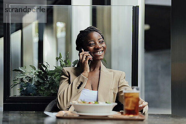 Glückliche Geschäftsfrau  die in der Cafeteria sitzt und mit dem Handy telefoniert