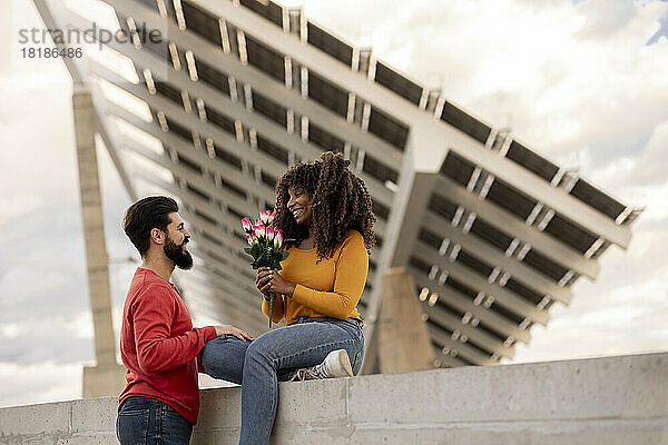Glücklicher Mann und Frau halten Blumenstrauß vor Sonnenkollektoren