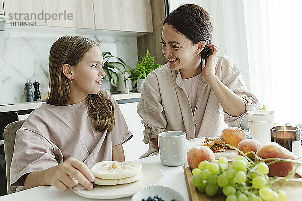 Glückliche Frau spricht mit Tochter am Esstisch in der Küche