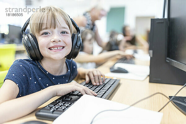 Happy elementary schoolgirl wearing headphones in computer class at school
