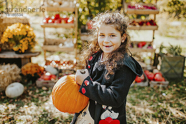Lächelndes Mädchen hält Kürbis auf der Herbstmesse an einem sonnigen Tag