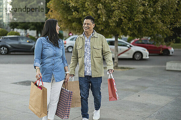 Glückliches älteres Paar mit Einkaufstüten  das auf dem Fußweg läuft