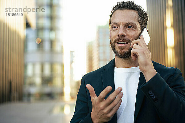 Lächelnder Geschäftsmann gestikuliert und spricht mit dem Mobiltelefon
