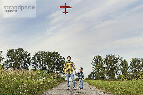 Vater und Sohn betrachten gemeinsam Modellflugzeug auf unbefestigter Straße