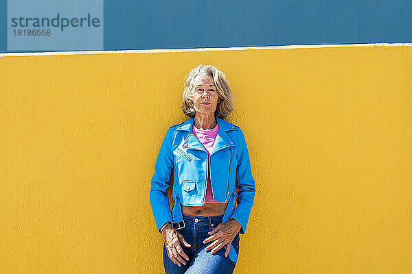 Reife Frau in blauer Lederjacke vor der Wand