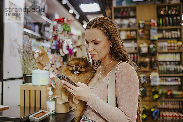Frau trägt Hund mit Smartphone in Tierhandlung