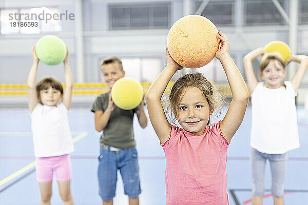Lächelndes Mädchen hält Ball auf dem Schulsportplatz mit Freunden im Hintergrund