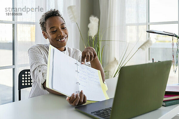 Lächelnder Junge  der zu Hause Notizen zu einem Videoanruf über einen Laptop zeigt