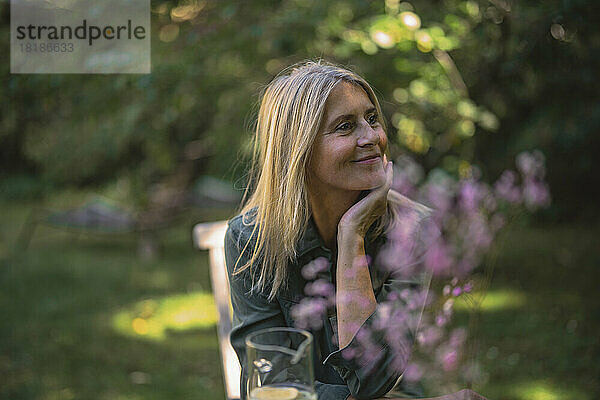 Lächelnde reife Frau mit der Hand am Kinn sitzt im Garten