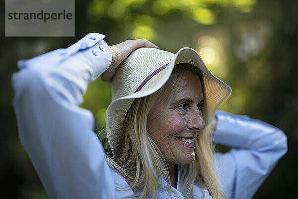 Smiling woman adjusting hat in garden