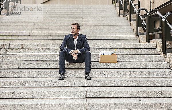 Trauriger Geschäftsmann sitzt mit Karton auf der Treppe