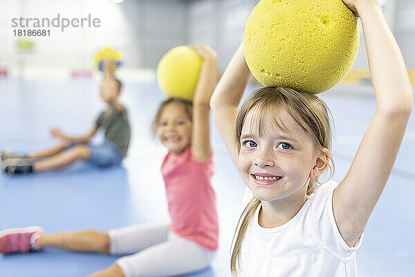 Smiling girl holding ball on head at school sports court