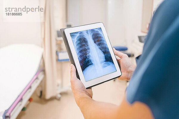 Hände eines Arztes halten einen Tablet-PC in der Hand und untersuchen das Röntgenbild im Krankenhaus