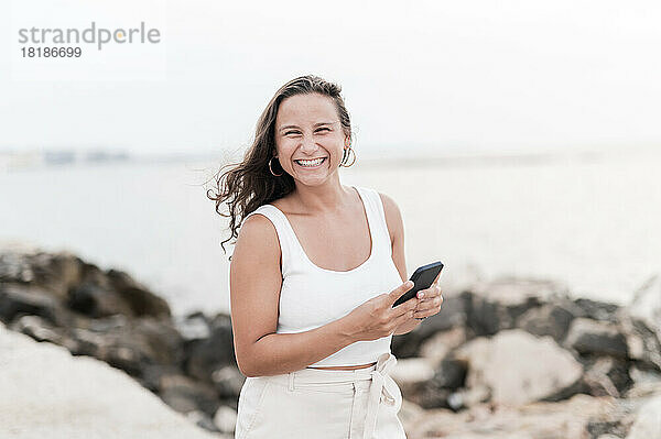 Glückliche junge Frau mit Handy genießt Strandurlaub