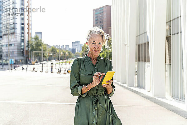 Reife Frau mit Smartphone auf Fußweg in der Stadt